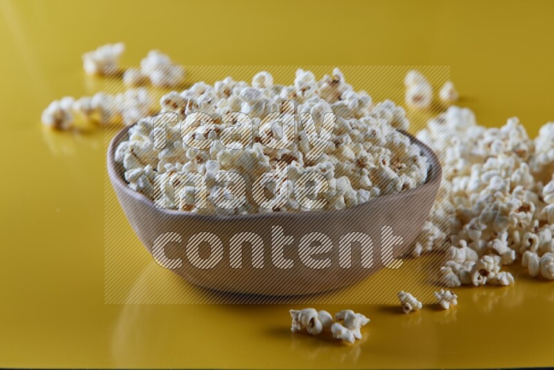 A brown pottery bowl full of popcorn with popcorn beside it on a yellow background in different angles