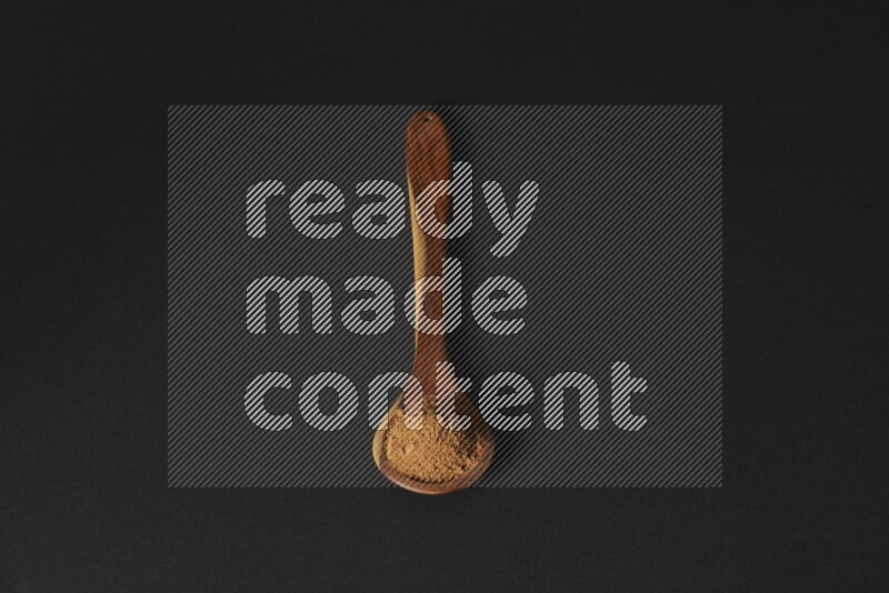 Cinnamon powder in a spoon ladle on black background