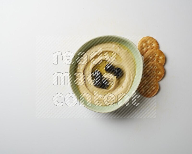 Hummus in a green plate garnished with black olives on a white background