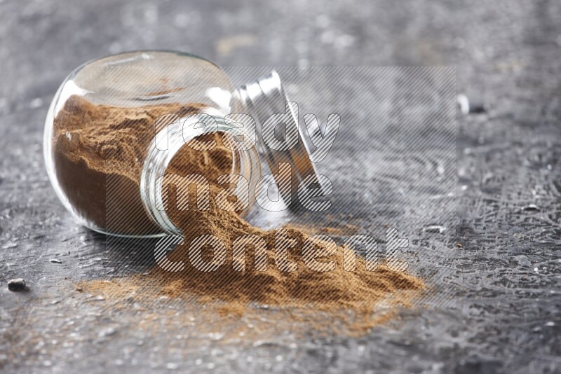 Flipped herbal glass jar full of cinnamon powder on textured black background