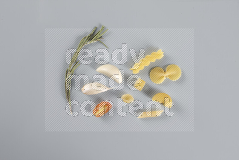 Raw pasta with different ingredients such as cherry tomatoes, garlic, onions, red chilis, black pepper, white pepper, bay laurel leaves, rosemary, cardamom and mushrooms on light blue background