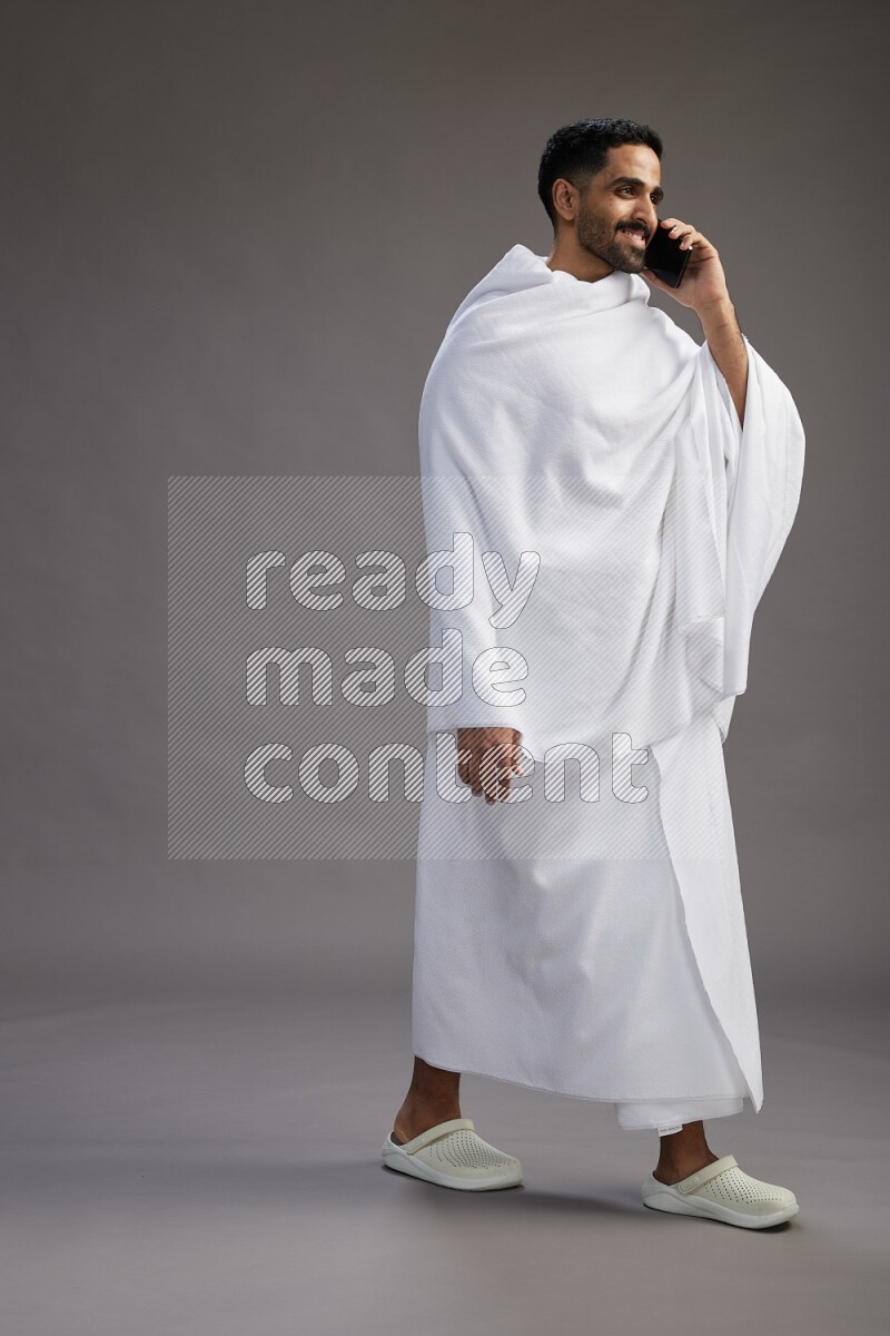 A man wearing Ehram Standing talking on phone on gray background