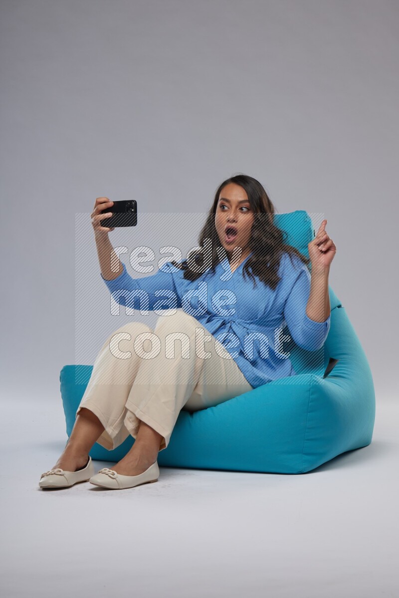 A woman sitting on a blue beanbag and taking selfie