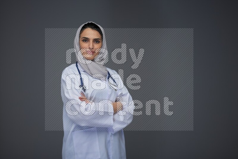 A female doctor wearing a light gray head scarf standing on grey background.
