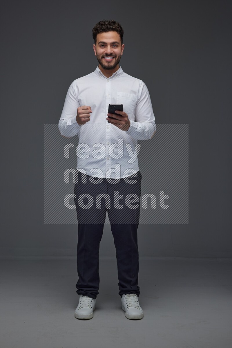 A man wearing smart casual standing and using his phone eye level on a gray background