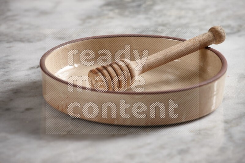 Beige Pottery Oven Bowl with wooden honey handle on the side with grey marble flooring, 15 degree angle
