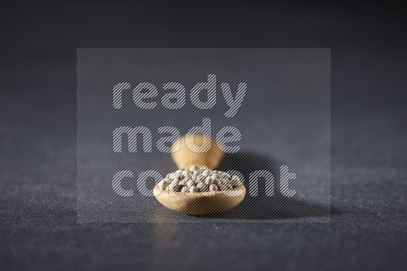 A wooden spoon full of white pepper beads on black flooring