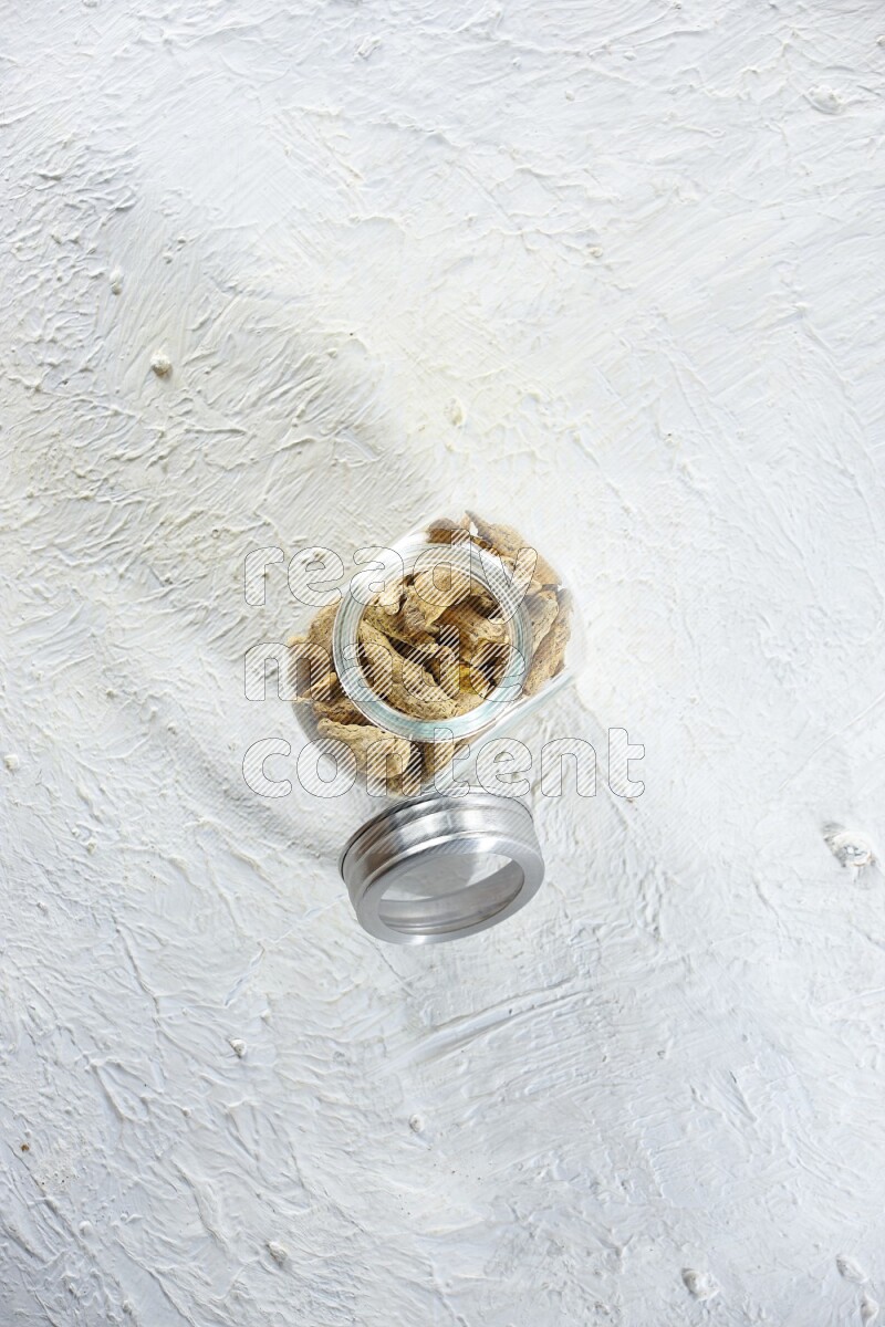 وعاء زجاجي للتوابل ممتلئ بأصابع الكركم المجففة على خلفية بيضاء