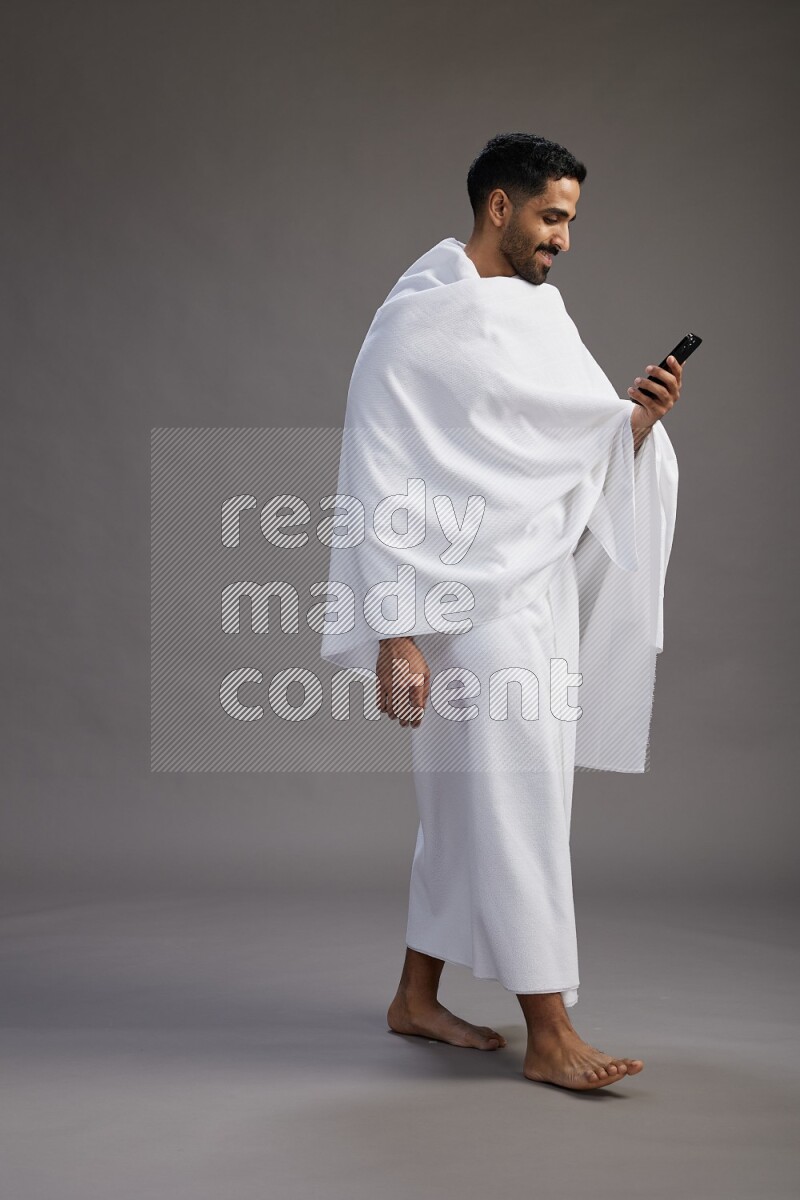 A man wearing Ehram Standing texting on phone on gray background