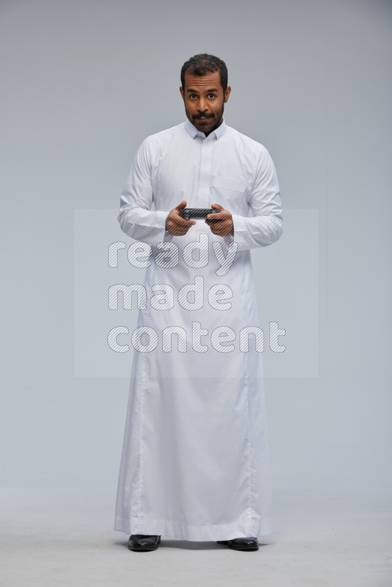 Saudi man Wearing thob standing holding joystick on Gray background
