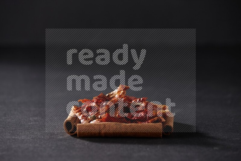 A single square of cinnamon sticks full of chilis on black flooring