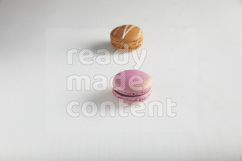 45º Shot of of two assorted Brown Irish Cream, and Purple Strawberry macarons on white background