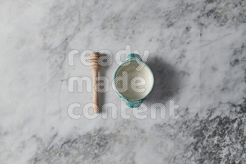 Multicolored pottery bowl with wooden honey dipper on the side on grey marble background