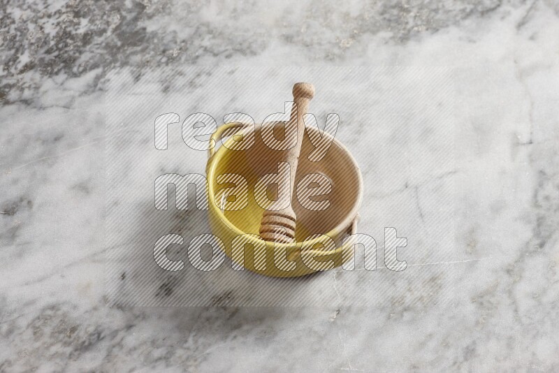 Multicolored pottery bowl with wooden honey dipper in it on grey marble background