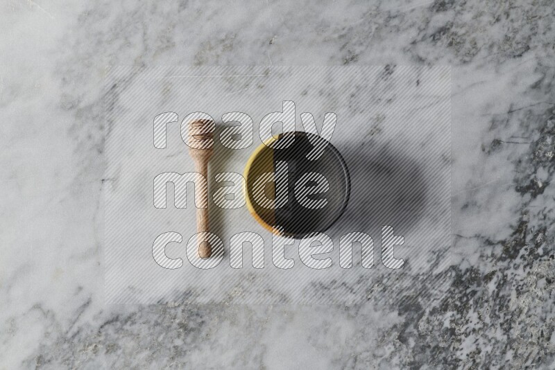 Multicolored pottery bowl with wooden honey dipper on the side on grey marble background