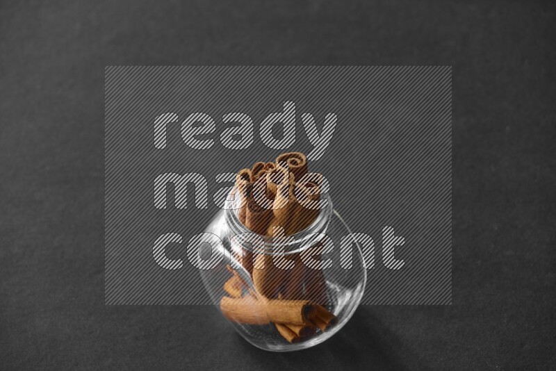 A glass spice jar full of cinnamon sticks on black flooring