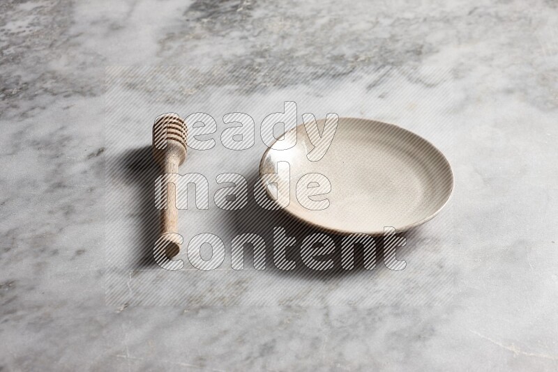 Beige pottery plate with wooden honey dipper on the side on grey marble background