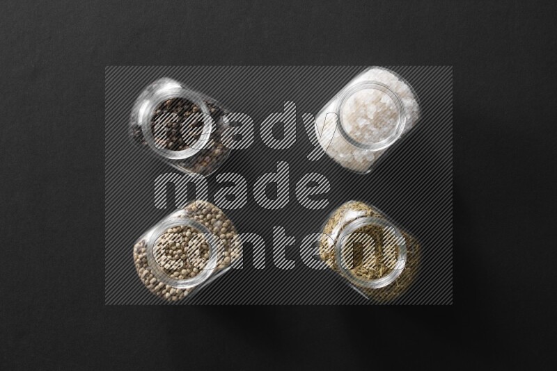 ملح وفلفل أسود وفلفل أبيض وكمون في أوعية زجاجية علي خلفية سوداء