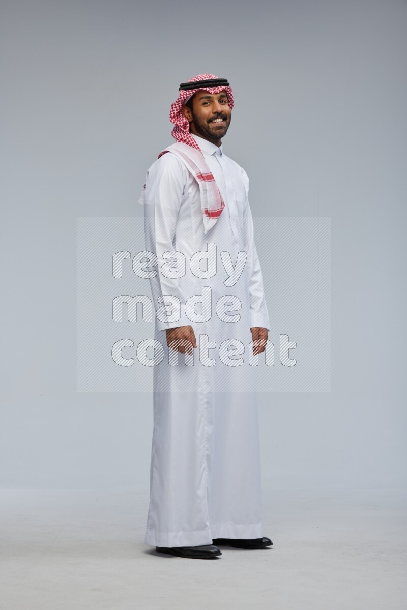 Saudi man Wearing Thob and shomag standing interacting with the camera on Gray background
