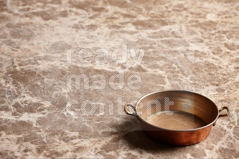 A small copper pan on beige marble background