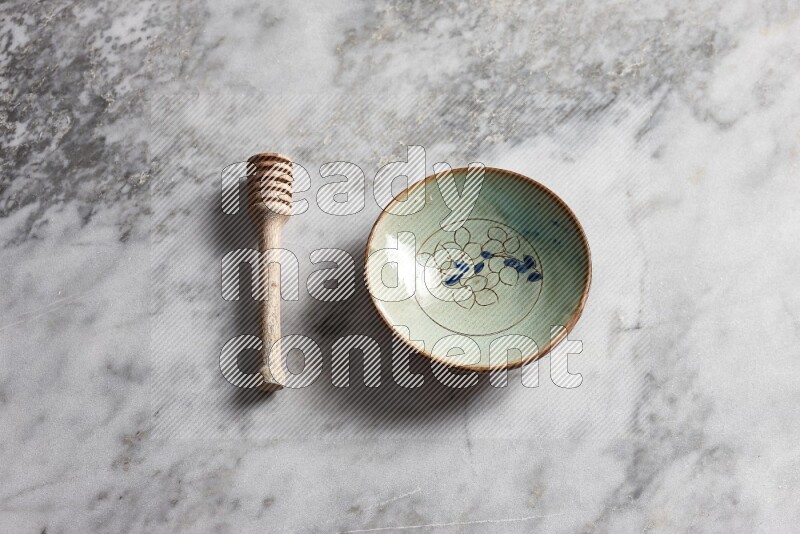 Decorative pottery plate with wooden honey dipper on the side on grey marble background