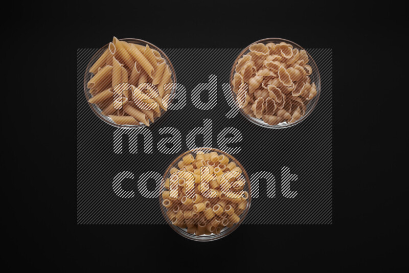 Different pasta types in glass bowls on black background