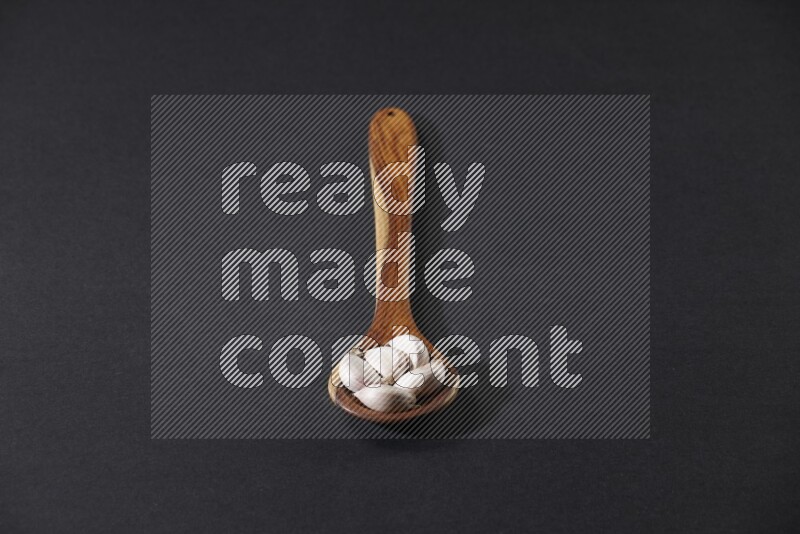 ملعقة خشبية كبيرة مليئة بفصوص الثوم على خلفية سوداء