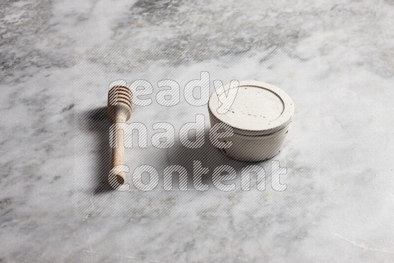 White pottery bowl with wooden honey dipper on the side on grey marble background