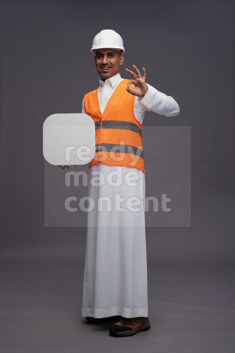 Saudi man wearing thob with engineer vest standing holding social media sign on gray background