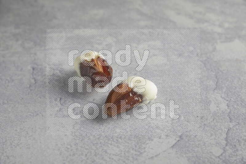 two almonds stuffed dates covered with white chololate on a light grey background