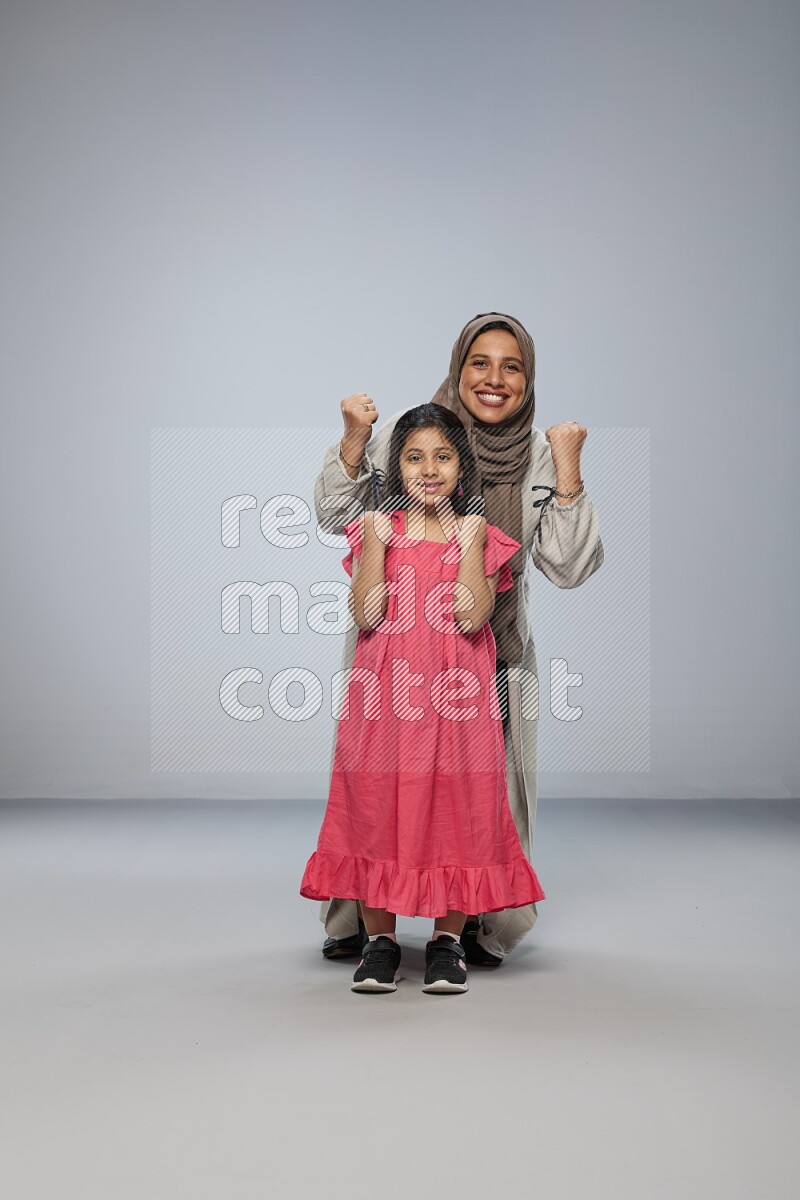A girl and her mother interacting with the camera on gray background