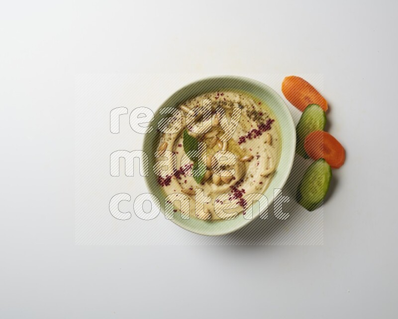 Hummus in a green plate garnished with zattar & sumak on a white background