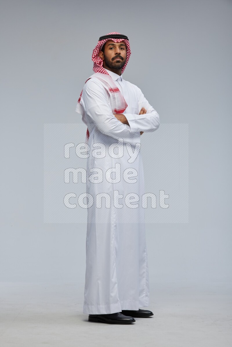Saudi man Wearing Thob and shomag standing with crossed arms on Gray background
