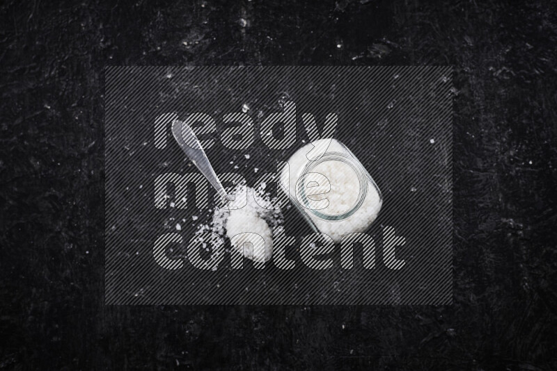 A glass jar full of coarse sea salt crystals on black background
