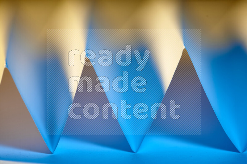 A close-up abstract image showing sharp geometric paper folds in blue gradients and warm tones