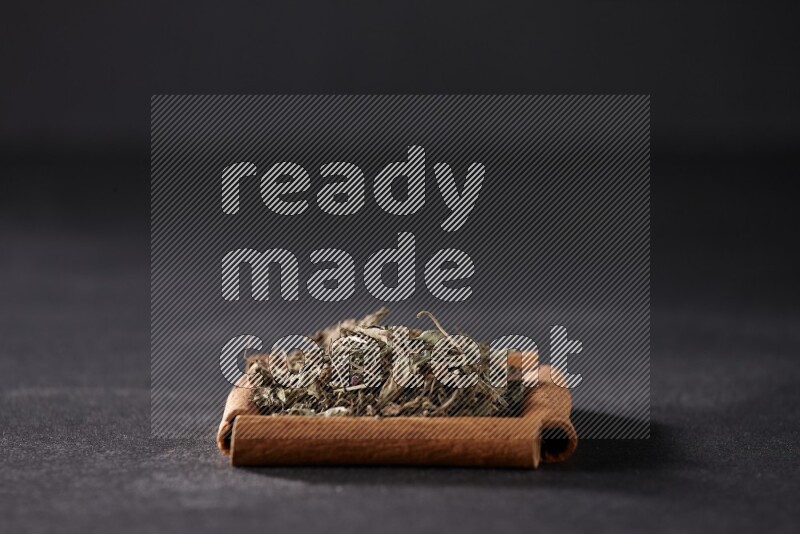 أربعة من أعواد القرفة مكونة شكل مربع بداخلها ريحان مجفف علي خلفية سوداء