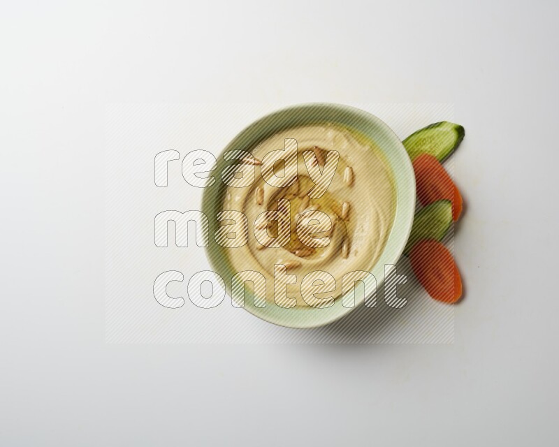 Hummus in a green plate garnished with pine nuts on a white background