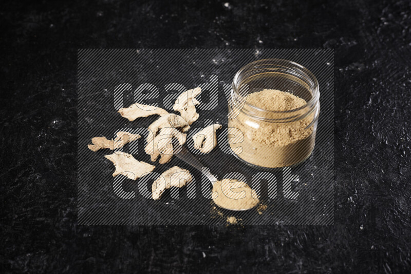 A glass jar full of ground ginger powder on black background