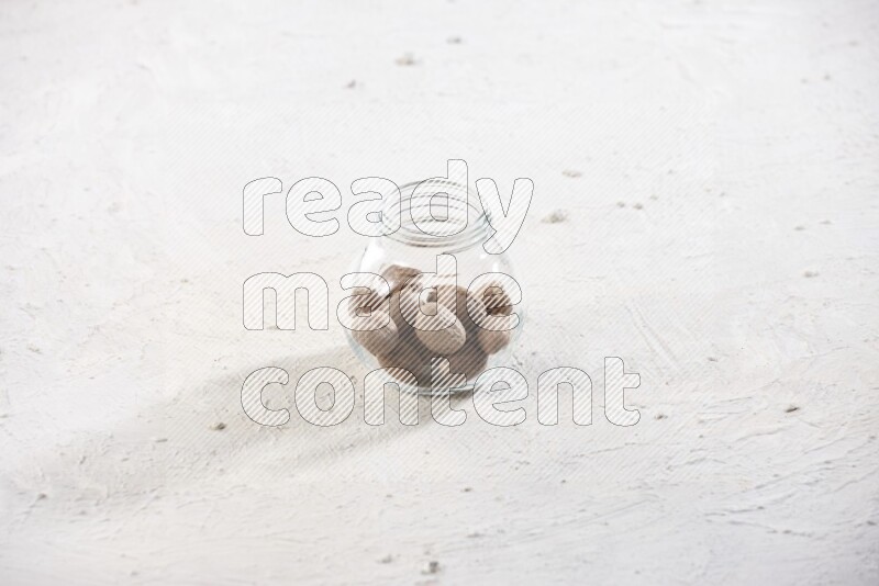 A glass spice jar full of whole nutmeg seeds on a textured white flooring