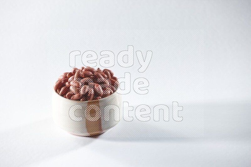 A beige ceramic bowl full of red skin peanuts on a white background in different angles