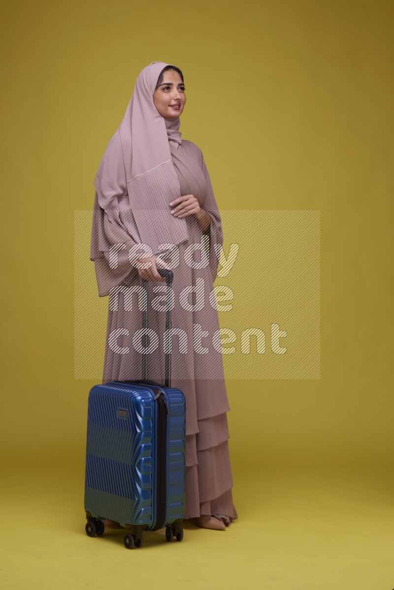 A woman With suit Case on a Yellow Background wearing Brown Abaya with Hijab