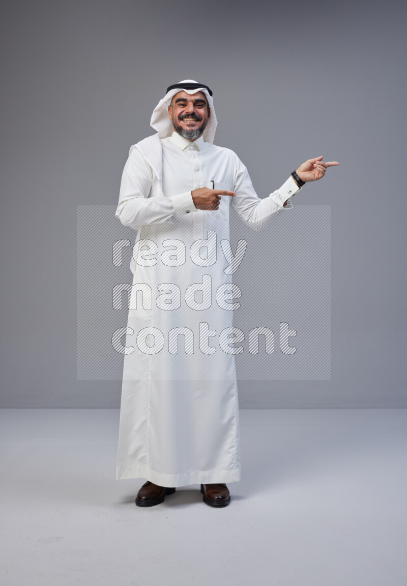 Saudi man Wearing Thob and white Shomag standing interacting with the camera on Gray background