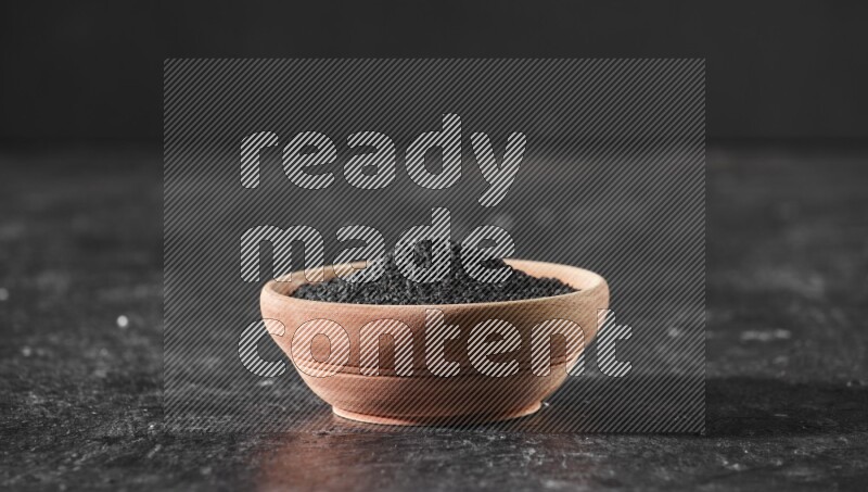 وعاء خشبي ممتلئ ببذور حبة البركة علي خلفية سوداء