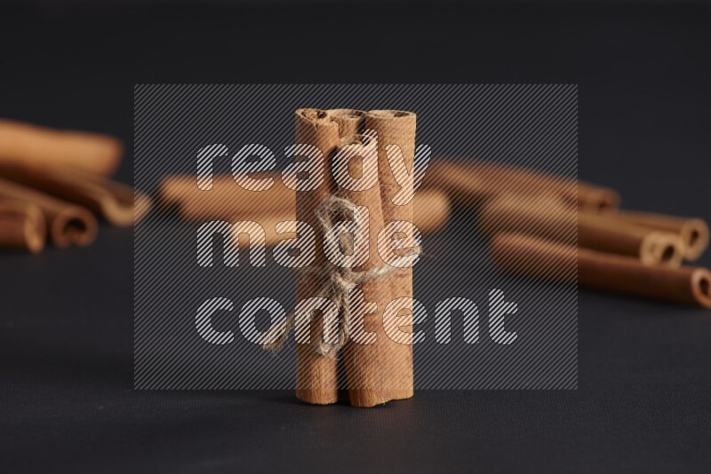 4 Cinnamon sticks stacked and bounded with more sticks in the background on black flooring
