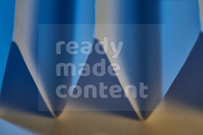 A close-up abstract image showing sharp geometric paper folds in blue gradients and warm tones