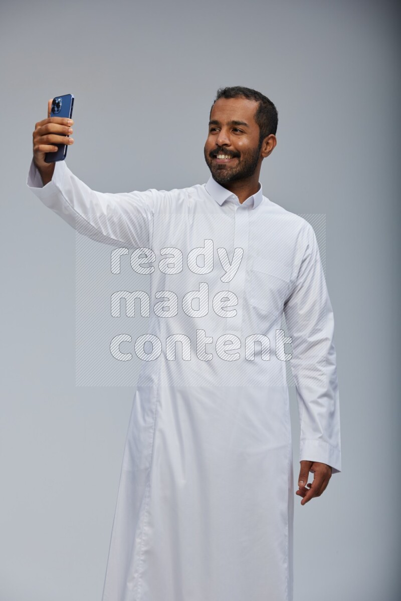 Saudi man wearing Thob standing taking selfie on Gray background