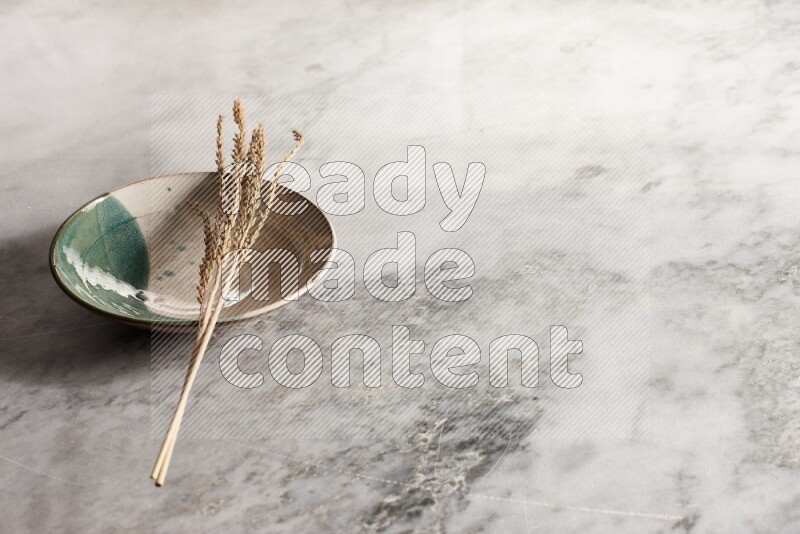 Wheat stalks on multicolored pottery plate on grey marble background
