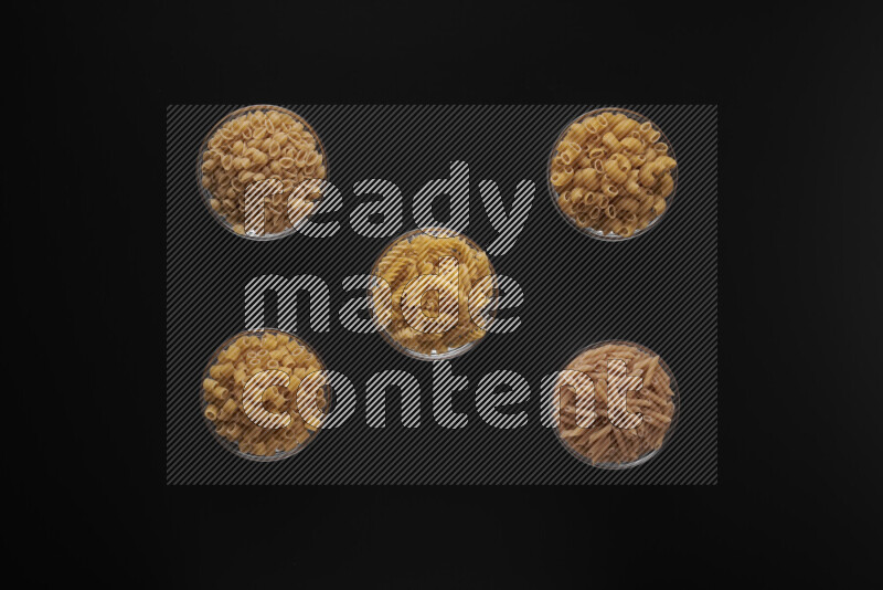 Different pasta types in 5 glass bowls on black background