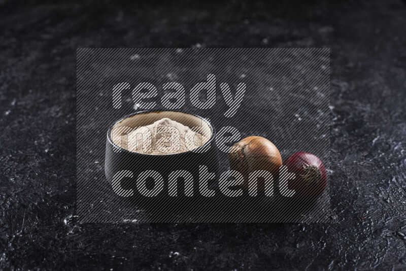 A black pottery bowl full of onion powder on black background