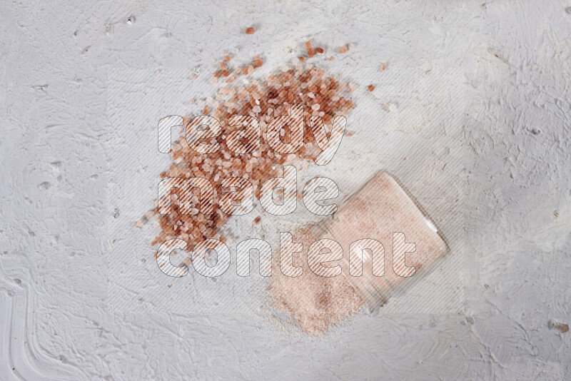 A glass jar full of fine himalayan salt with some himalayan crystals beside it on a white background